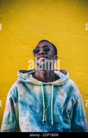 Portrait of young man wearing sunglasses leaning against yelow wall Stock Photo