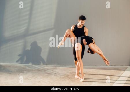 Professional male dancer helping female gymnast in dance pose against wall Stock Photo