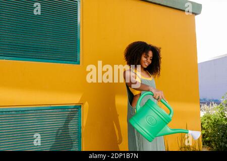 Young woman wearing overalls watering flowers in garden Stock Photo
