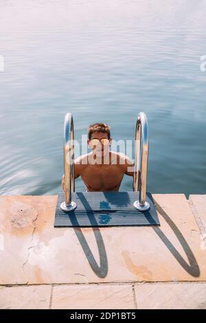 Portrait of young man wearing sunglasses getting out of the water Stock Photo