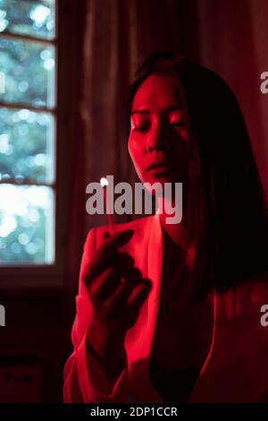 Woman holding burning matchstick in low red light at home Stock Photo