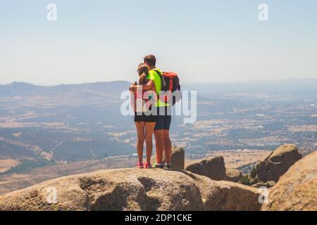 Couple of hikers in sportswear are on a big rock taking a break and looking at the valley on a sunny summer day Stock Photo