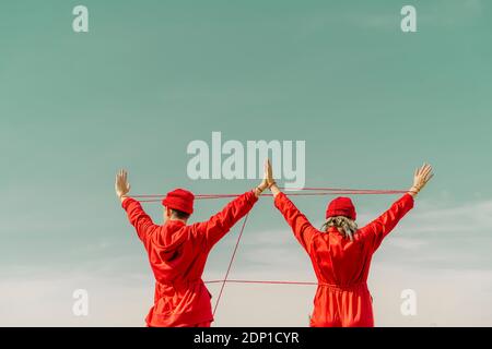 Back view of young couple wearing red overalls and hats performing with red string outdoors Stock Photo