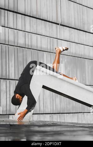 Young man wearing black kaftan performing on concrete structure outdoors Stock Photo