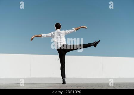 Back view of ballet dancer with headphones practising on roof terrace Stock Photo
