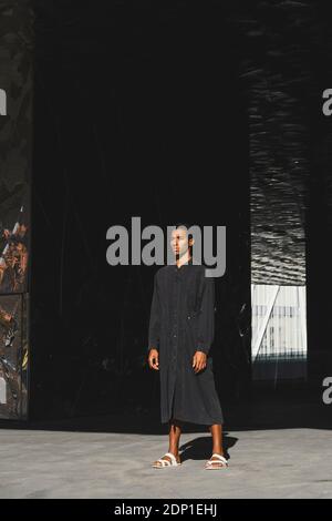 Young man wearing black kaftan standing outdoors Stock Photo