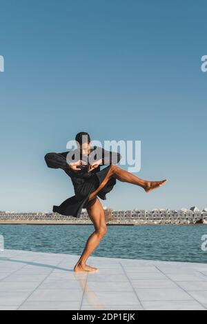 Young man wearing black kaftan performing at the waterfront Stock Photo