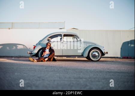 Senior man sitting in front of vintage car using mobile phone Stock Photo
