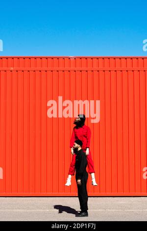 Young couple in overalls performing in  front of red roller shutter Stock Photo