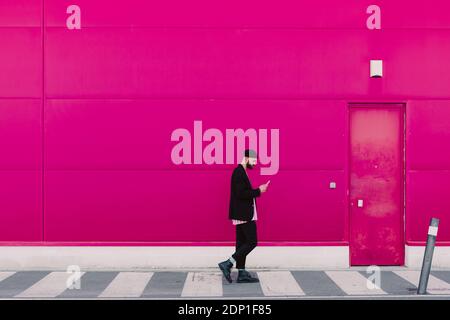 Businessman using smartphone and walking along a pink wall Stock Photo