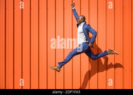 Businessman jumping in the air in front of orange wall Stock Photo