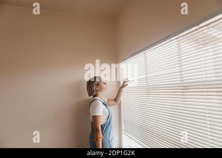 Young woman looking through blinds at the window Stock Photo