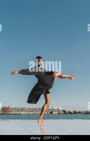 Young man wearing black kaftan performing at the waterfront Stock Photo