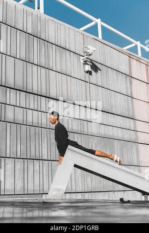 Young man wearing black kaftan performing on concrete structure outdoors Stock Photo