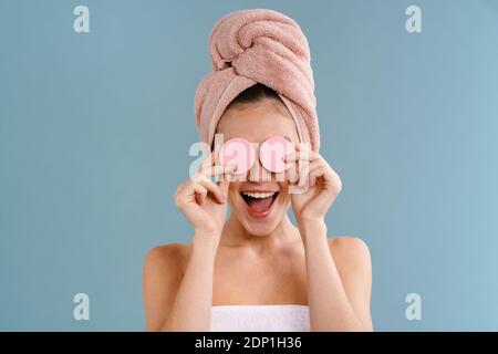 Nice excited girl wearing towels making fun with cosmetic sponges isolated over blue background Stock Photo