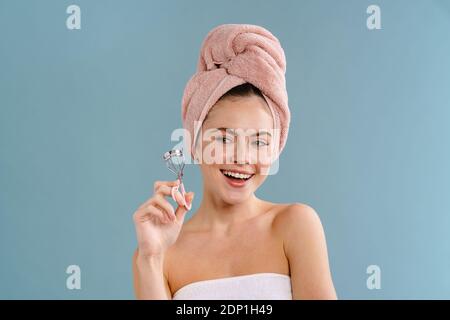Nice happy girl wearing towels posing with eyelashes curler isolated over blue background Stock Photo
