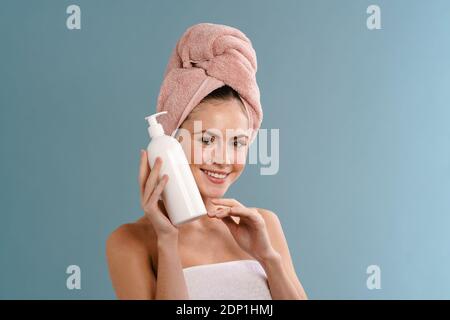 Nice happy girl wearing towels posing with body lotion isolated over blue background Stock Photo
