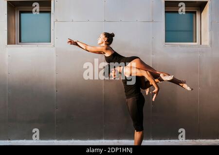 Male gymnast carrying female on shoulders while practicing dance posture by wall Stock Photo