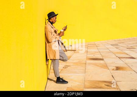Young man with hat, using smartphone, drinking coffee Stock Photo
