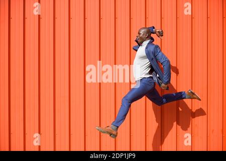 Businessman jumping in the air in front of orange wall Stock Photo
