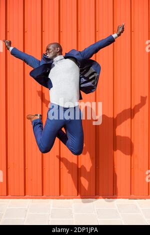 Successfull businessman jumping in the air in front of orange wall Stock Photo