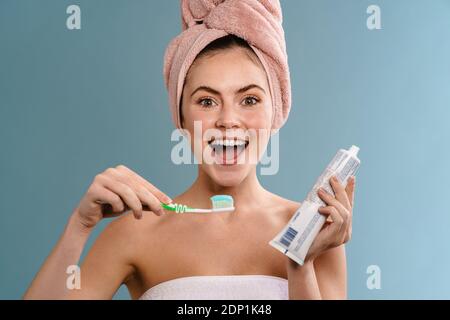 Nice excited girl wearing towels posing with toothpaste and toothbrush isolated over blue background Stock Photo