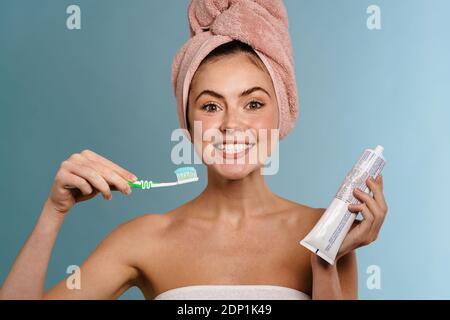 Nice excited girl wearing towels posing with toothpaste and toothbrush isolated over blue background Stock Photo
