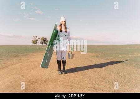 Young woman carrying green painting on dry field Stock Photo
