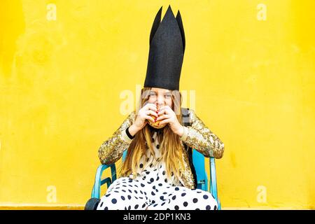 Portrait of girl wearing black crown eating Hamburger Stock Photo