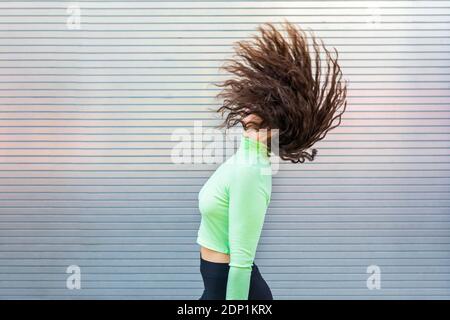 Young woman tossing hair while standing by gray wall Stock Photo