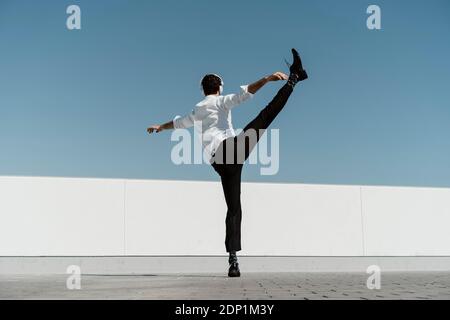 Back view of ballet dancer with headphones practising on roof terrace Stock Photo