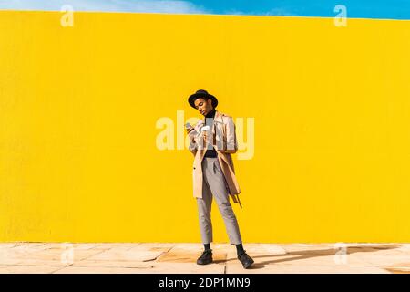 Young man with hat, using smartphone, drinking coffee Stock Photo