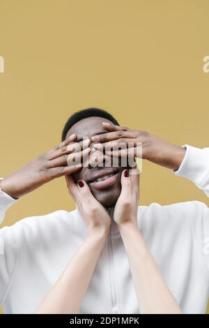 Portrait of smiling man covering eyes with his hands, touched by woman's hands Stock Photo