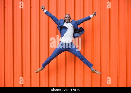 Happy businessman jumping in the air in front of orange wall Stock Photo