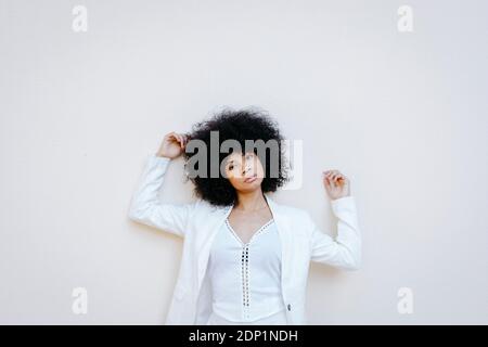 Portrait of African American woman with afro hair dressed in white suit in front of white urban wall in Granada, Spain Stock Photo