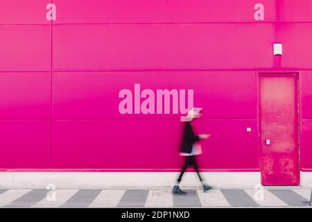 Young man with headphones walking along a pink wall, blurred Stock Photo