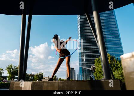 Sporty woman exercising with plastic hoops in modern city against blue sky Stock Photo
