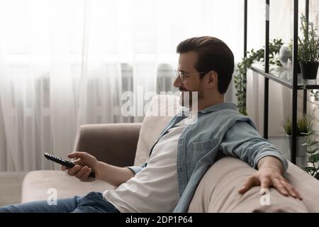 Relaxed young man watching tv choosing channel using remote control Stock Photo
