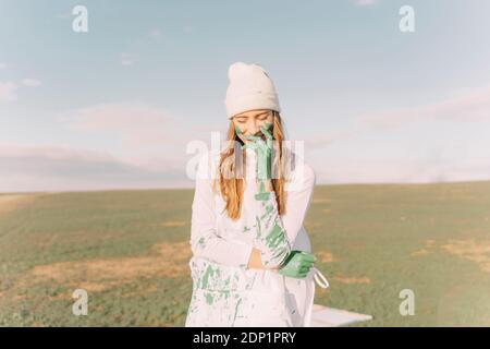 Young woman putting green painted hand on her face Stock Photo