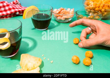 Hand of man playing with cheese puffs on table set with various snacks, appetizers and alcohol Stock Photo