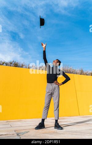Young man with black hat, dancing in front of yellow wall Stock Photo
