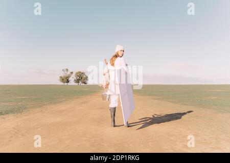 Young woman carrying easel and empty canvas on dry field Stock Photo