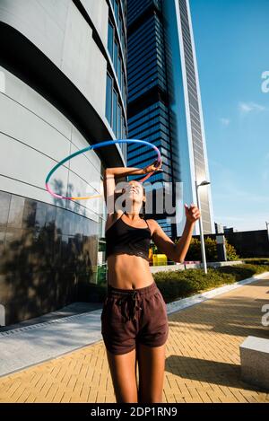 Sporty woman exercising with plastic hoops on sidewalk outside office buildings Stock Photo