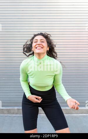 Cheerful young woman dancing against gray wall in city Stock Photo