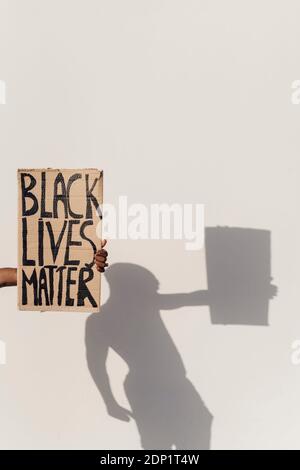 Hand holding Black Lives Matter sign, shadow of person on the wall Stock Photo
