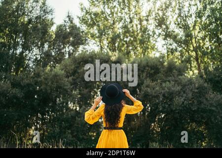 Rear view of a young woman wearing black hat and yellow dress enjoying nature Stock Photo