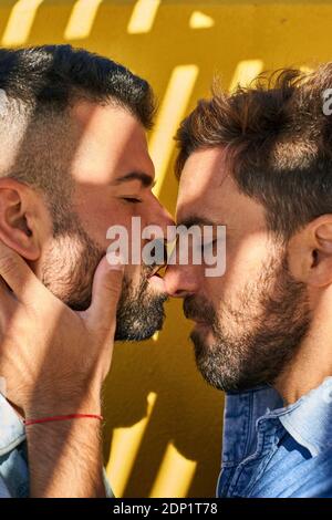 Gay couple doing romance while standing against yellow wall Stock Photo