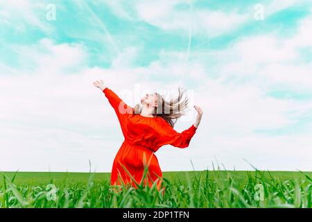 Happy woman wearing red dress dancing in a field Stock Photo