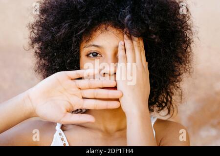 Portrait of African American woman with afro hair with hands on her face in front of old urban wall in Granada, Spain Stock Photo