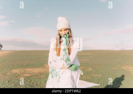 Young woman putting green painted hand on her face Stock Photo